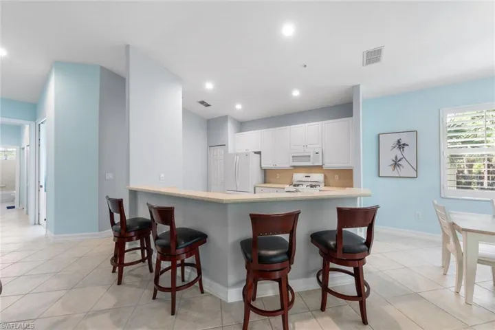 Kitchen featuring white cabinets, white appliances, backsplash, a breakfast bar, and light tile patterned flooring