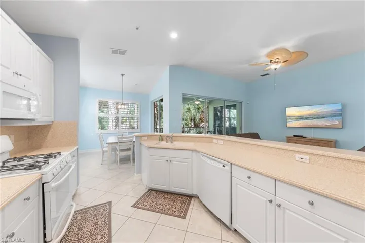 Kitchen featuring pendant lighting, white appliances, light tile patterned floors, ceiling fan, and white cabinets