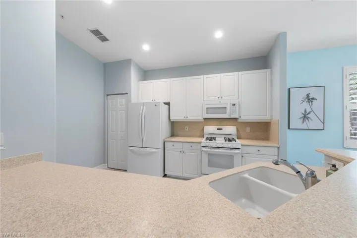 Kitchen with backsplash, sink, white appliances, and white cabinets