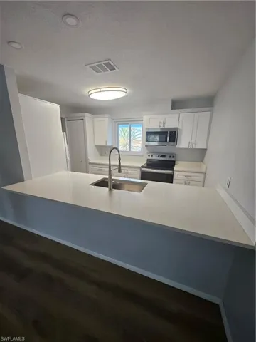 Kitchen with white cabinetry, sink, range, kitchen peninsula, and a textured ceiling