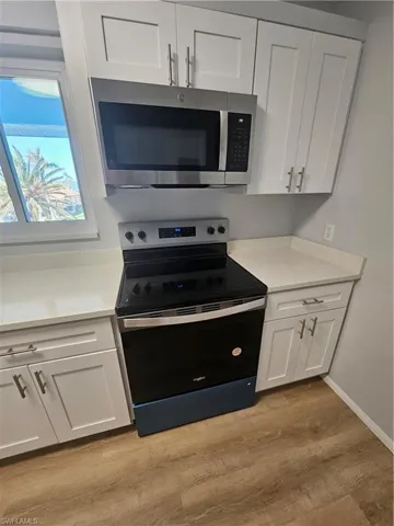 Kitchen with light stone counters, light hardwood / wood-style flooring, stainless steel range with electric cooktop, and white cabinets