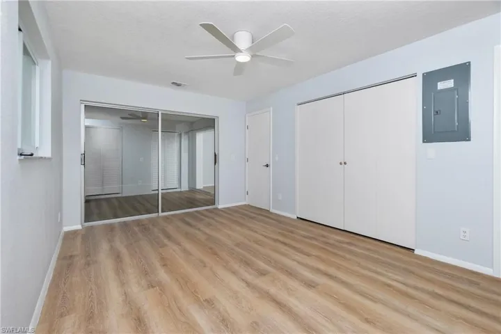 Unfurnished bedroom with ceiling fan, electric panel, light hardwood / wood-style floors, a textured ceiling, and multiple closets