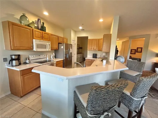Kitchen featuring a kitchen breakfast bar, kitchen peninsula, white appliances, and light tile floors