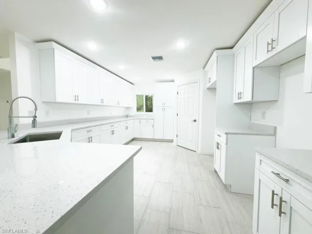 Kitchen featuring light stone countertops, sink, and white cabinets