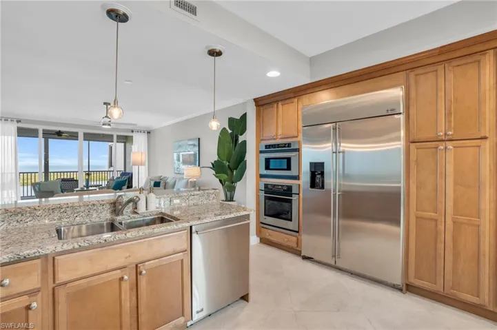 Kitchen featuring stainless steel appliances, hanging light fixtures, sink, and light stone counters