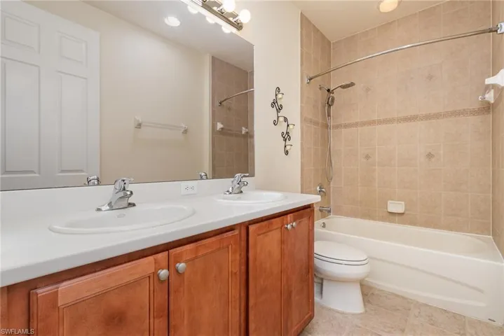 Full bathroom #4 featuring vanity with dual sink, tile patterned floors, toilet, and tiled shower / and bath vinyl bathtub.