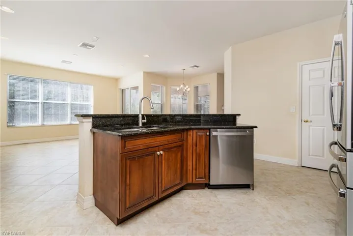 Kitchen with sink, dark stone countertops, hanging light fixtures, light tile patterned floors, and stainless steel appliances