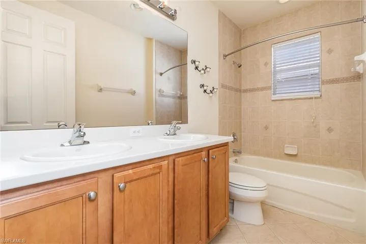 Full bathroom #3 with vanity with dual sink, tile patterned floors, toilet, and tiled shower / and bath vinyl bathtub.