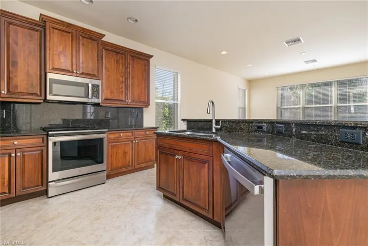 Kitchen with sink, stainless steel appliances, an breakfast bar with sink, decorative backsplash, and dark stone counters.