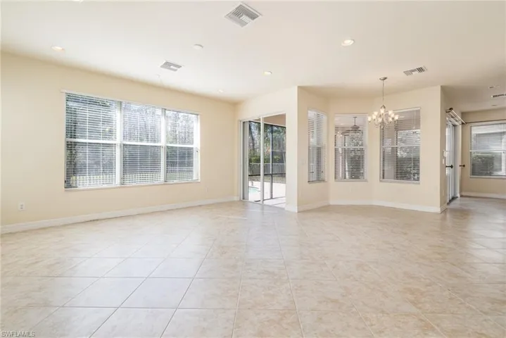 Spacious room featuring an inviting chandelier and light tile patterned floors and view to the pool and preserve.