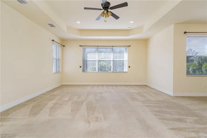 Carpeted bedroom featuring ceiling fan and a raised tray ceiling. Views to pool and preserve on the back of the house.