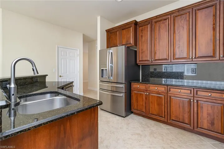 Kitchen featuring stainless steel refrigerator with ice dispenser, backsplash, sink, and dark stone countertops.