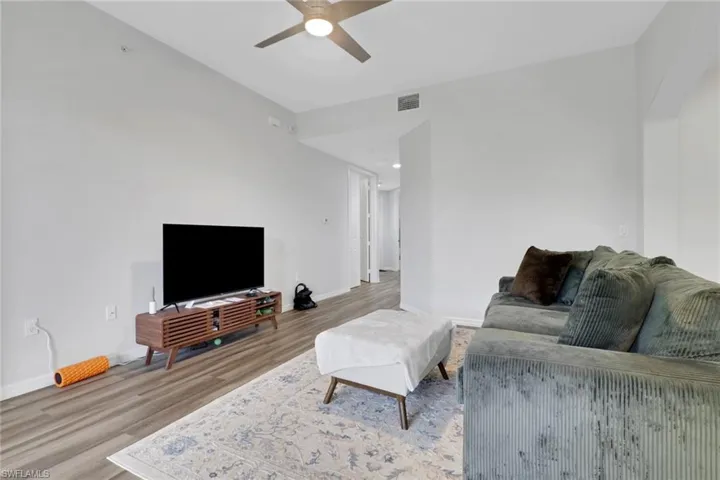 Spacious living area featuring wood-finish flooring, light gray wall paint, and a ceiling fan with integrated lighting