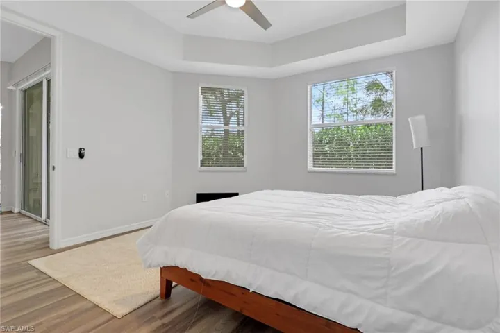 Room featuring wood-finish flooring, a tray ceiling with a ceiling fan, and two windows with blinds