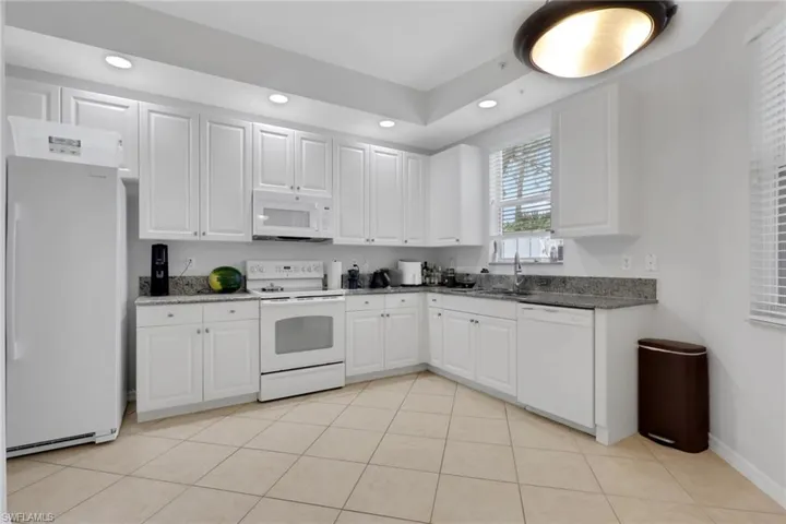 Kitchen featuring extensive white cabinetry, speckled granite countertops, a white appliance suite, recessed lighting, and large format tile flooring