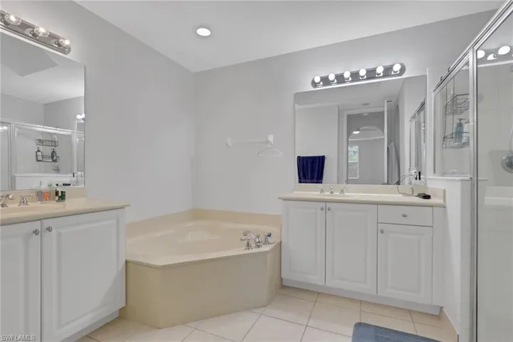 Bathroom featuring a corner soaking tub, dual vanity with white cabinetry, light-toned countertops, and a glass-enclosed shower