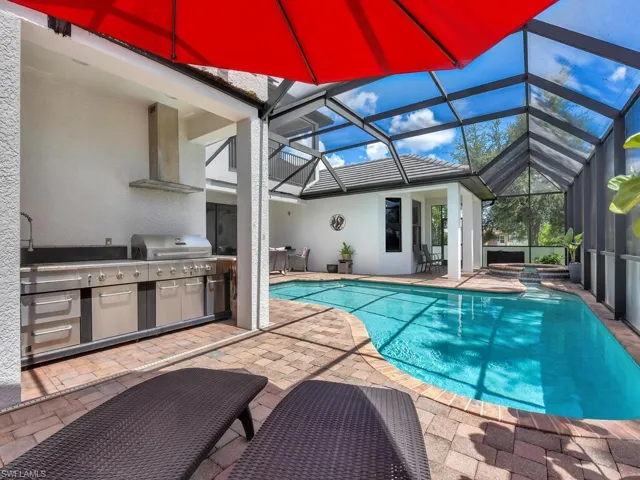View of pool with glass enclosure, exterior kitchen, grilling area, and a patio