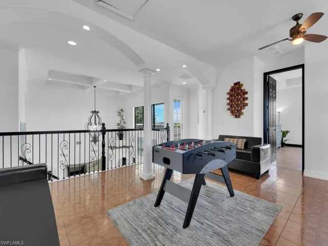 Recreation room with tile patterned floors, decorative columns, and ceiling fan with notable chandelier