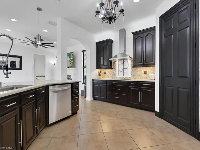 Kitchen featuring sink, hanging light fixtures, stainless steel dishwasher, wall chimney exhaust hood, and tasteful backsplash