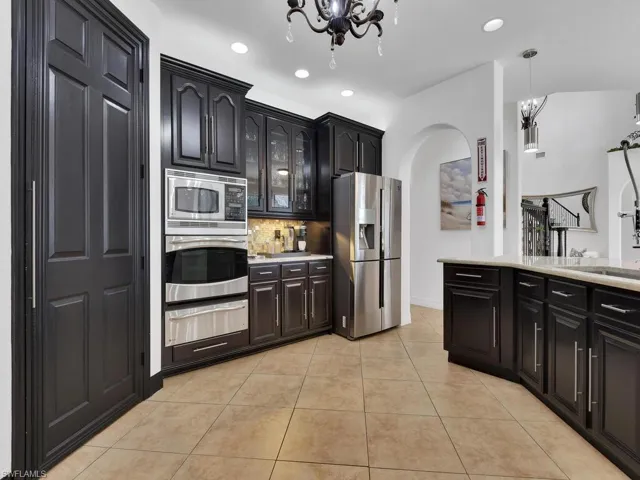 Kitchen with decorative backsplash, stainless steel appliances, an inviting chandelier, hanging light fixtures, and light tile patterned flooring