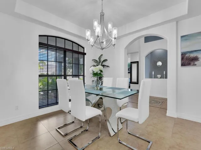 Dining space featuring a raised ceiling, light tile patterned flooring, and an inviting chandelier