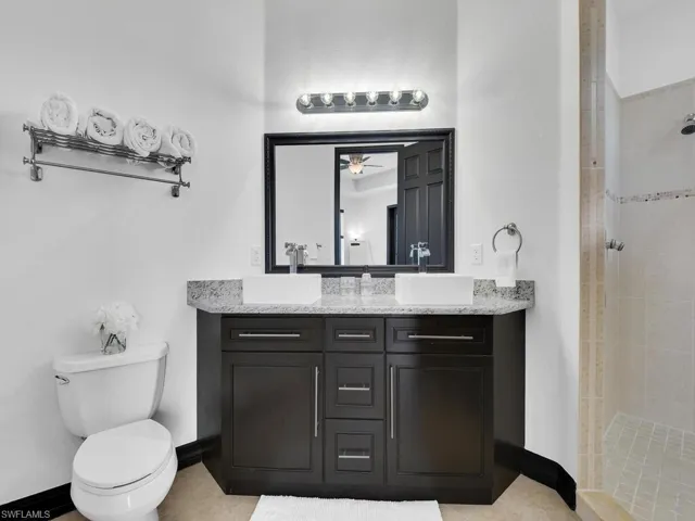 Bathroom with ceiling fan, tile patterned flooring, toilet, tiled shower, and vanity