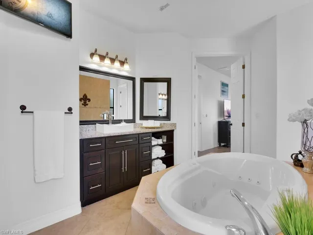 Bathroom featuring tile patterned flooring, vanity, and a relaxing tiled tub