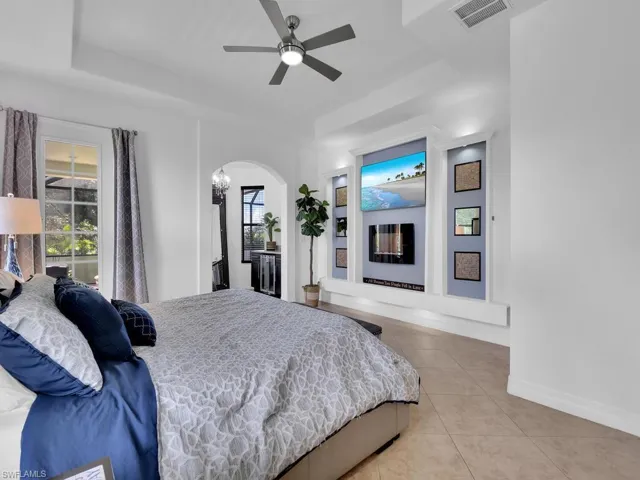 Bedroom featuring a tray ceiling, light tile patterned floors, and ceiling fan with notable chandelier