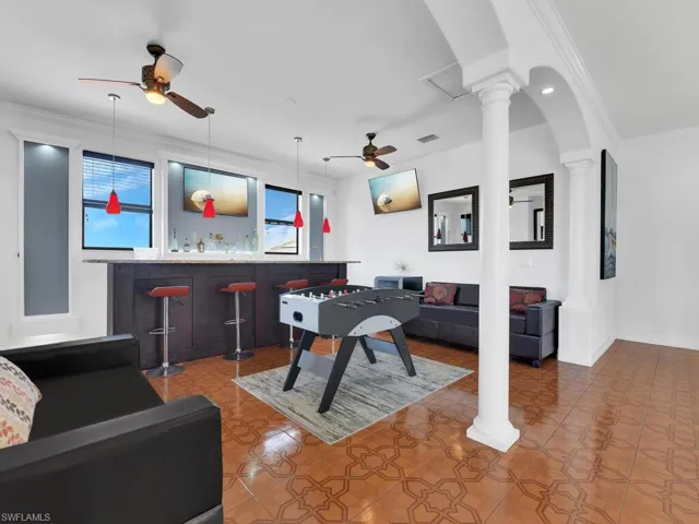Recreation room with decorative columns, tile patterned floors, and crown molding
