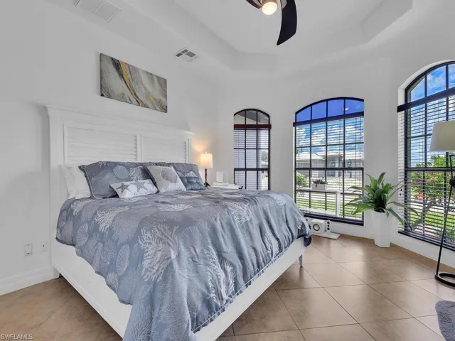 Tiled bedroom featuring ceiling fan, a towering ceiling, and a tray ceiling