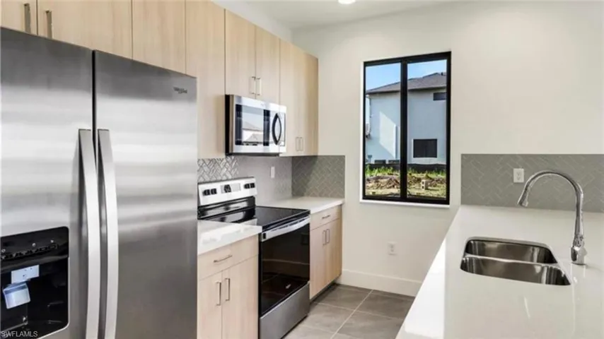 Kitchen featuring stainless steel appliances, decorative backsplash, light brown cabinets, light stone countertops, and modern cabinets
