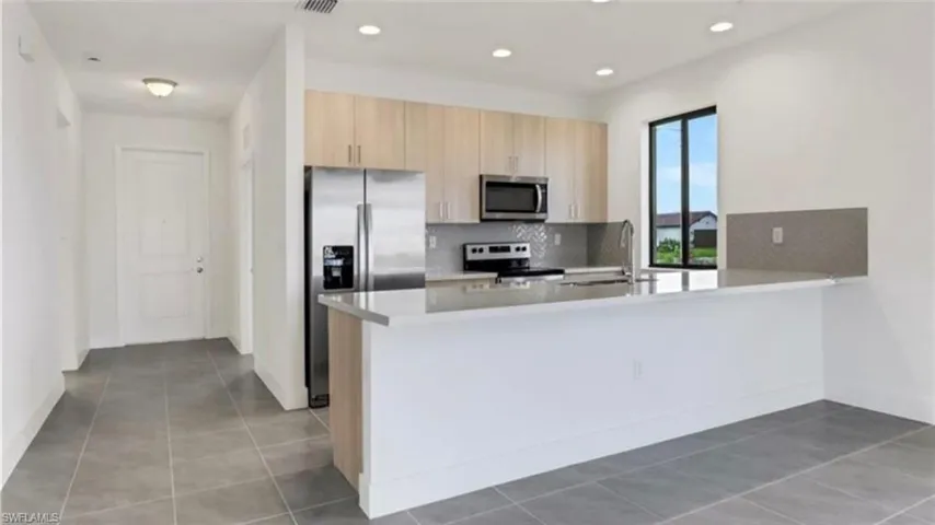 Kitchen with a peninsula, stainless steel appliances, light brown cabinets, light tile patterned floors, and recessed lighting