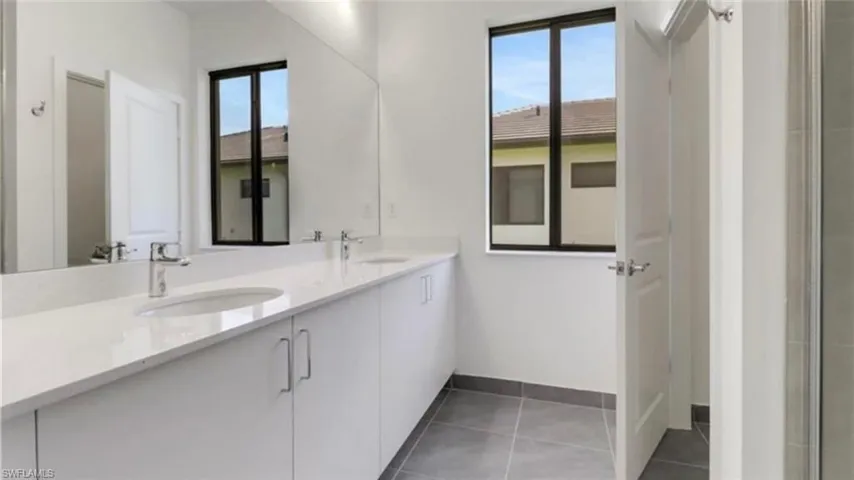 Full bath featuring double vanity, dark tile patterned flooring, and an enclosed shower