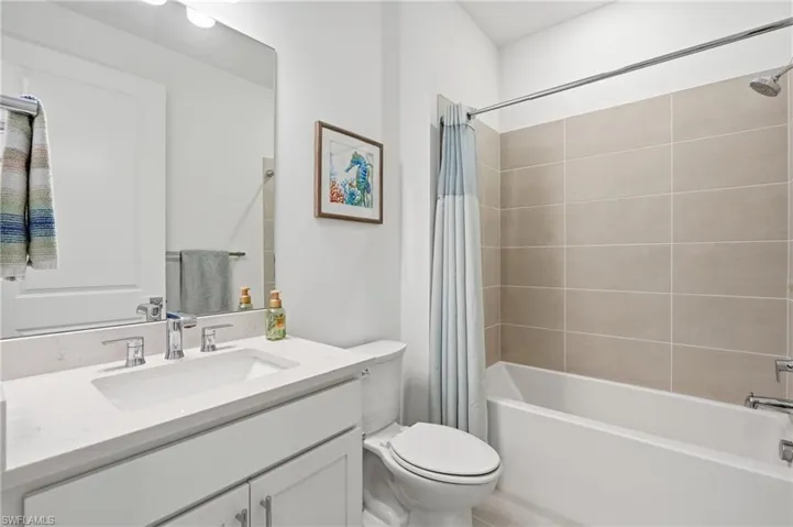 Bathroom featuring a white vanity with an integrated sink and chrome fixtures, a full-width mirror, and a bathtub with neutral-toned tiled surround