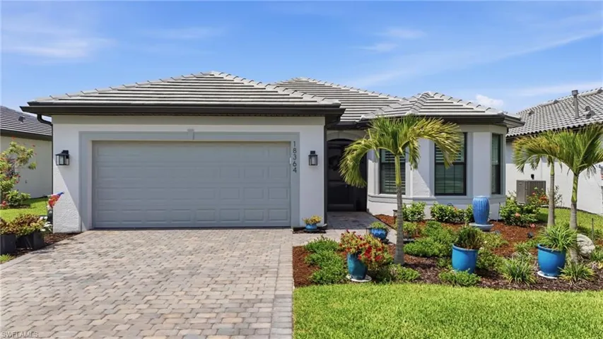 Contemporary stucco exterior with a tile roof, paver driveway, and a two-car garage