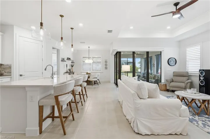 Open-concept living area featuring a large kitchen island with pendant lighting, a tray ceiling, recessed lighting, expansive glass sliding doors, and light-toned tile flooring