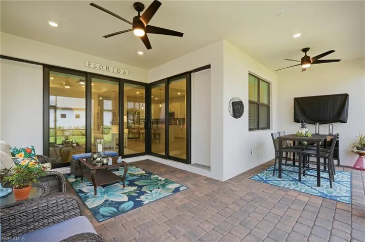 Expansive covered patio featuring a paver flooring, multiple ceiling fans, recessed lighting, and large sliding glass doors providing access to the interior