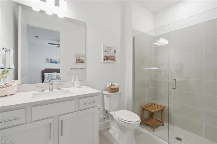 Bathroom featuring a large glass-enclosed shower with tile surround, a single vanity with a white countertop and undermount sink, white cabinetry with silver-tone hardware, and an overhead vanity light fixture