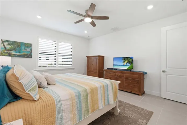 Bedroom featuring neutral-toned tile flooring, white walls, and a multi-blade ceiling fan with integrated lighting