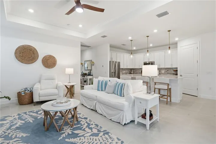 Open-concept living space featuring a tray ceiling with recessed lighting and a ceiling fan, large format tile flooring, and an integrated kitchen with white cabinetry, stainless steel appliances, and pendant lighting