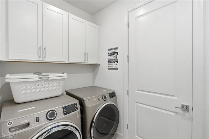 Laundry area featuring white shaker-style cabinetry with chrome pulls, a solid white door with brushed nickel hardware, and light-toned walls