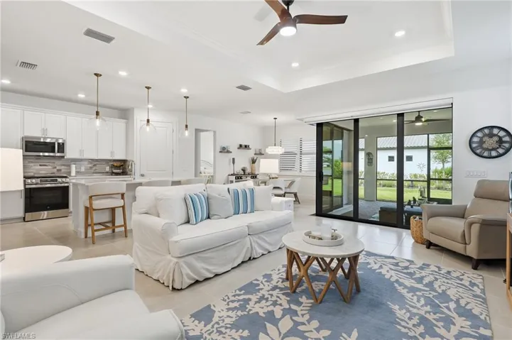 Open-concept living area with large format tile flooring, a tray ceiling, and ceiling fan