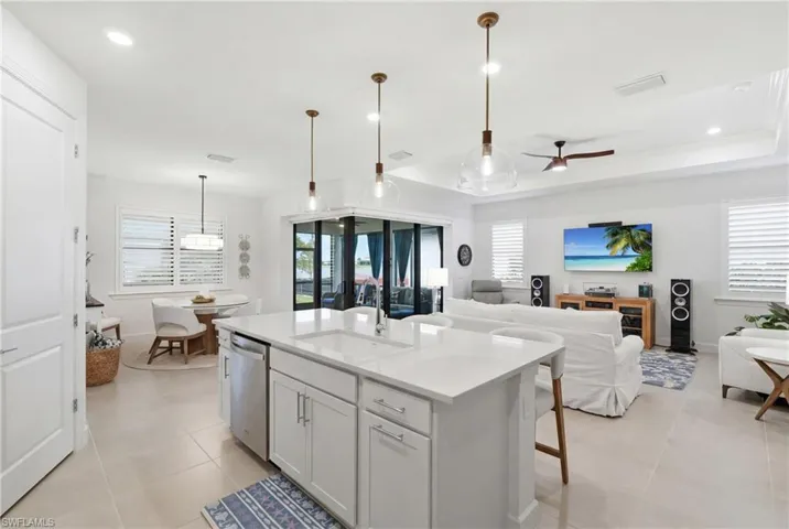 Open-concept living space with large format tile flooring, a kitchen island featuring a sink and dishwasher, white cabinetry, and recessed lighting