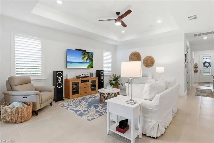 Living area featuring a tray ceiling with recessed lighting and ceiling fan, plantation shutters, and light-toned tile flooring