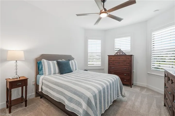Bedroom featuring a neutral carpet, multiple windows with white plantation shutters, and a contemporary ceiling fan with integrated lighting