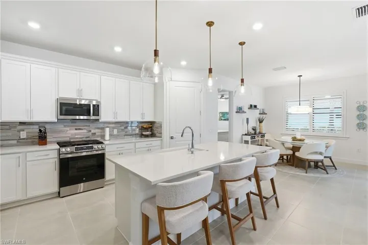 Modern kitchen featuring white cabinetry, stainless steel appliances, a white island with pendant lighting, and light-toned tile flooring