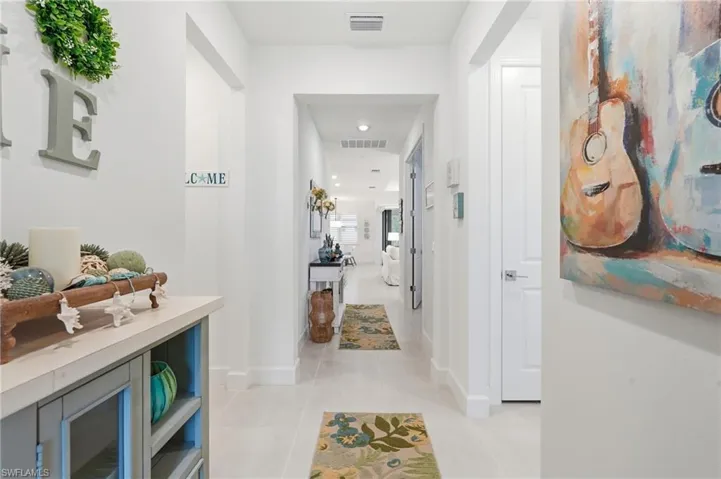 Long hallway with light-toned tile flooring, recessed lighting, and white baseboards