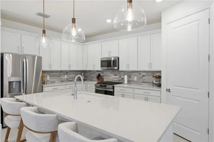 Kitchen featuring a large central island with seating, white shaker-style cabinetry, stainless steel appliances, a tile backsplash, and pendant lighting