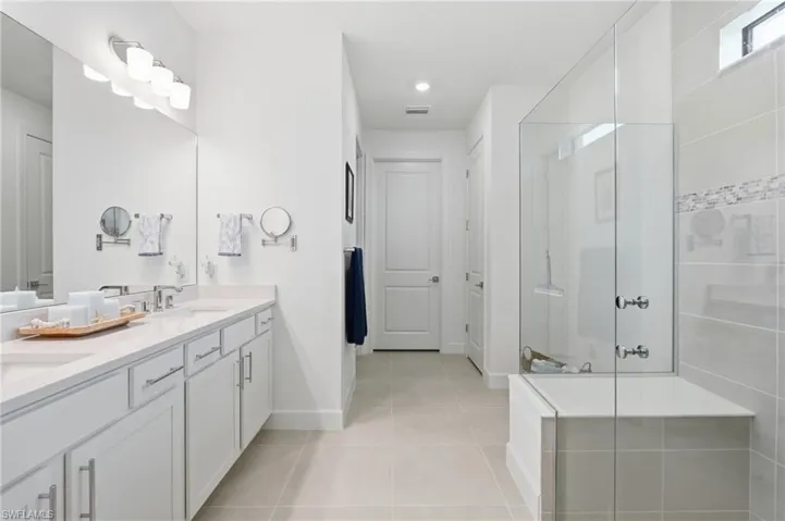 Dual vanity with integrated sinks, a full-width mirror, and a frameless glass shower enclosure with a built-in tub