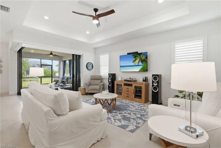 Living area with large format tile flooring, tray ceiling with recessed lighting, and a ceiling fan